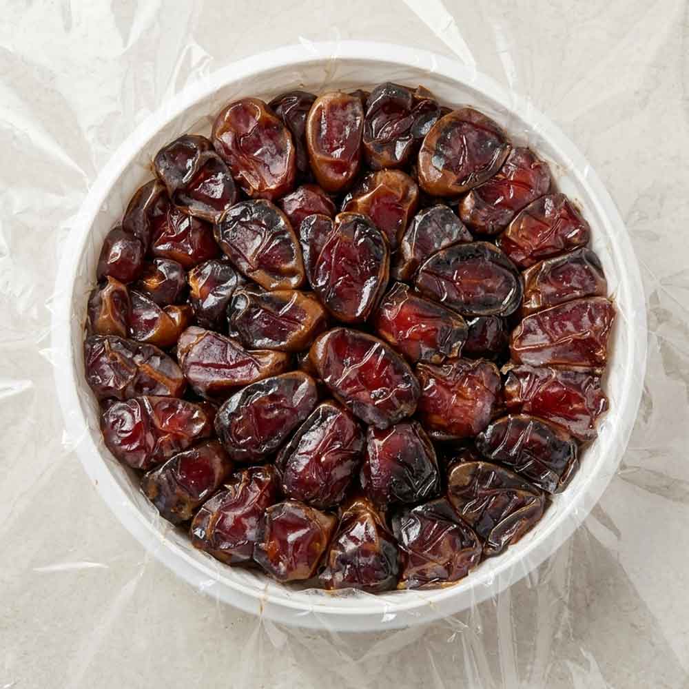 نمای از بالا از چیدمان فشرده دانه‌های درشت و شیره‌دار خرمای کبکاب در ظرف دایره‌ای